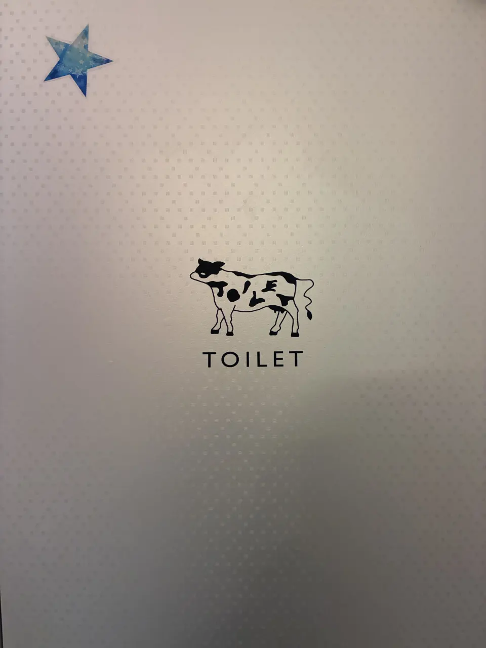 ぶち模様がTOILETの文字になっている牛のトイレサイン。シルバーの扉に黒のカッティングシート